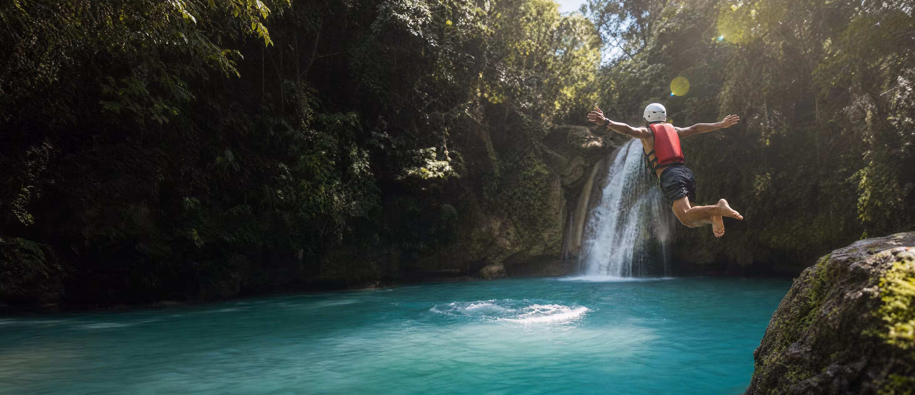A traveler in a red life vest leaps into a turquoise canyon pool at Kawasan Falls
